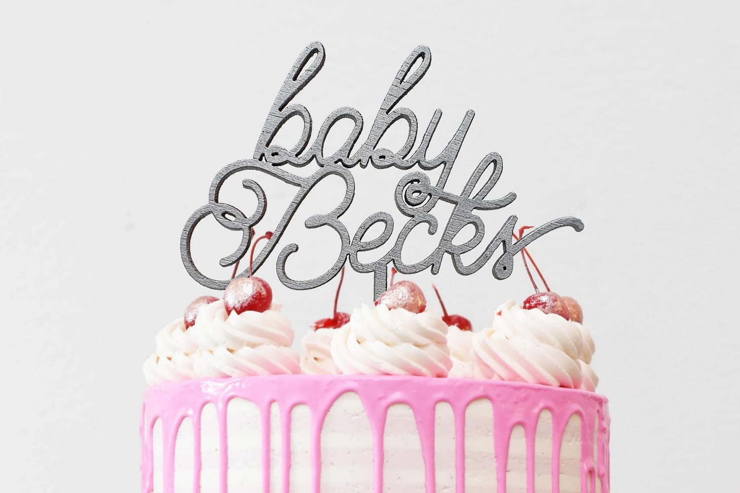Taarttopper met baby en gepersonaliseerd met de achternaam van de baby op een roze drip cake